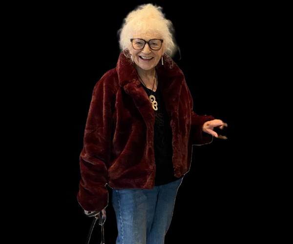 Patt smiles vibrantly at the camera as she reaches for a dark door. 